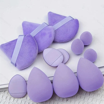 A set of purple makeup sponges in various shapes and sizes, including teardrop, round, and wedge shapes. 